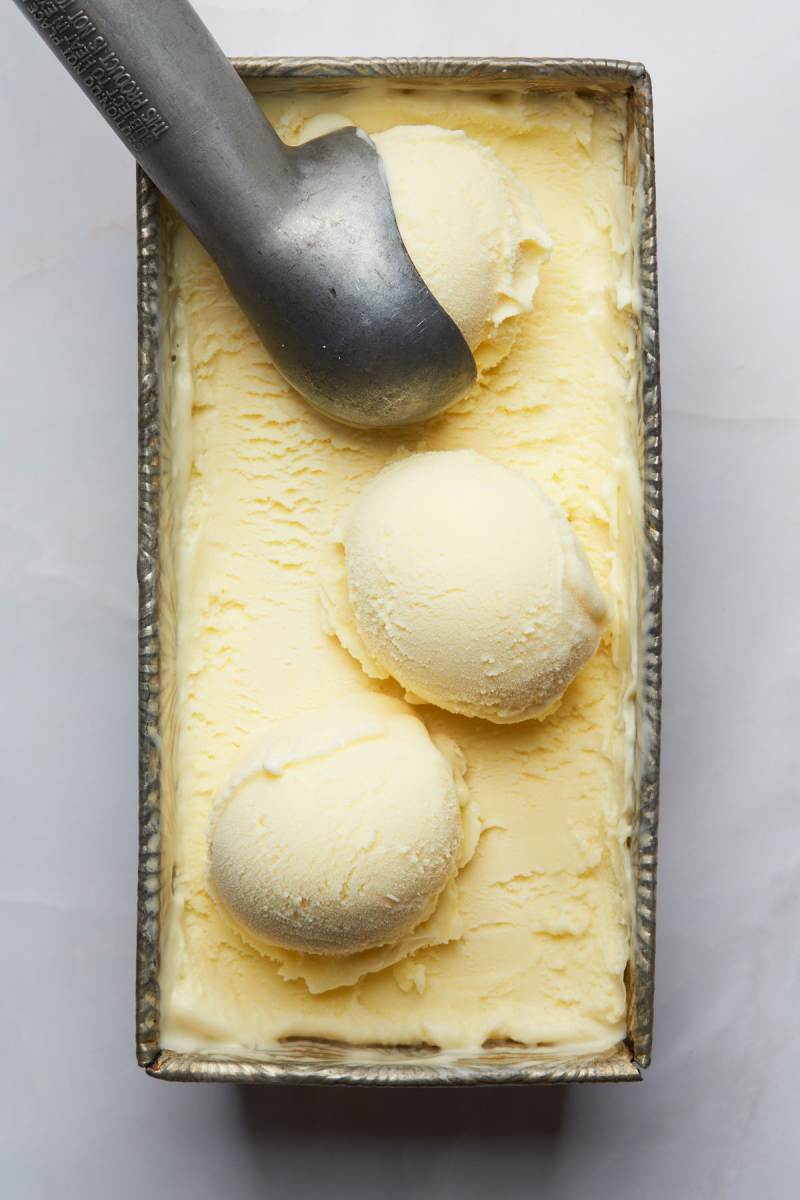 A metal scoop and scoops of ice cream in a metal tin